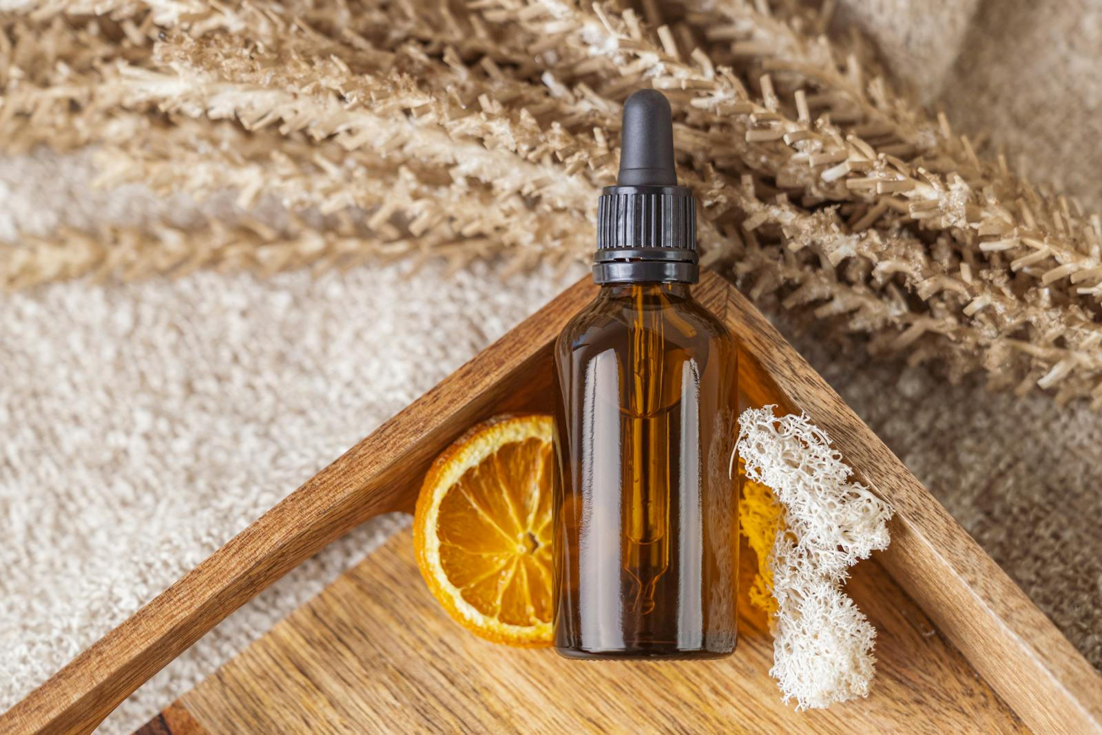 A natural face serum bottle with an orange slice on a wooden tray featuring dried botanicals.